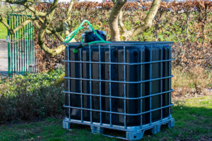 watertank 1000 liter-vernieuwd-pallet-metaal-of-kunststof-zijaanzicht-achteraanzicht-met-uitgaande-slang-in-tuinomgeving-300x200