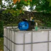 ibc-container-wit-met-pomp-220V-1000L-gereinigd-pallet-metaal-of-kunststof-linkeraanzicht-vooraanzicht-in-tuinomgeving.webp