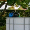 ibc-container-wit-met-pomp-220V-1000L-gereinigd-pallet-metaal-of-kunststof-vooraanzicht-in-tuinomgeving.webp