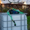 ibc-container-wit-met-pomp-accu-1000L-gereinigd-pallet-metaal-of-kunststof-linkerzijaanzicht-tuinomgeving-met-slang.webp