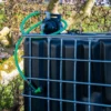 ibc-container-zwart-met-pomp-220V-1000L-vernieuwd-pallet-metaal-of-kunststof-zijaanzicht-achteraanzicht-met-uitgaande-slang-in-tuinomgeving.webp