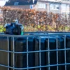 ibc-container-zwart-met-pomp-accu-1000L-vernieuwd-pallet-metaal-of-kunststof-vooraanzicht-zijaanzicht-zonder-uitgaande-slang.webp