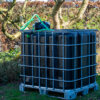 ibc-container-zwart-met-pomp-accu-1000L-vernieuwd-pallet-metaal-of-kunststof-zijaanzicht-achteraanzicht-met-uitgaande-slang-in-tuinomgeving.jpg