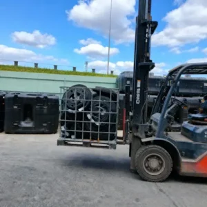 Heftruck gebruikt de kooi van een IBC container als transportbak voor putdeksels, met voorraad tanks op de achtergrond