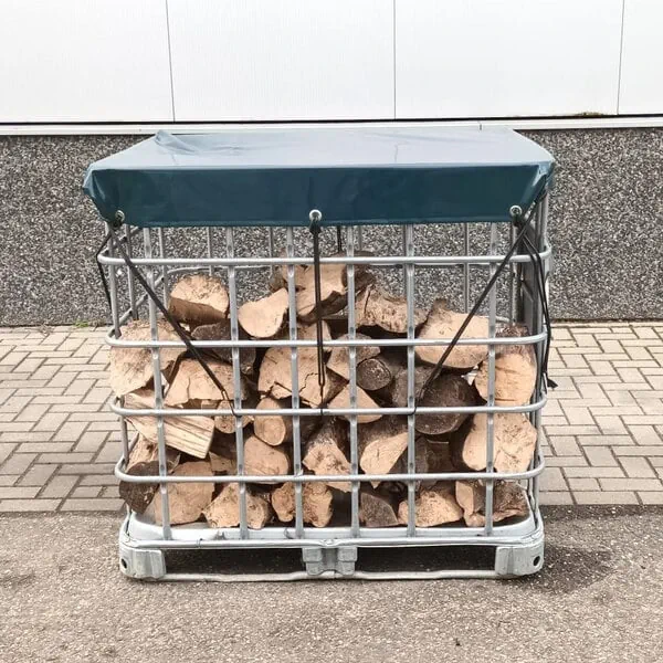 IBC container voor houtopslag buiten in de tuin, gevuld met droog brandhout en afgedekt met zeil