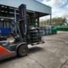 Kooi van een IBC container ingezet als transportbak voor putdeksels, verplaatst met heftruck op buitenterrein met opslagtanks